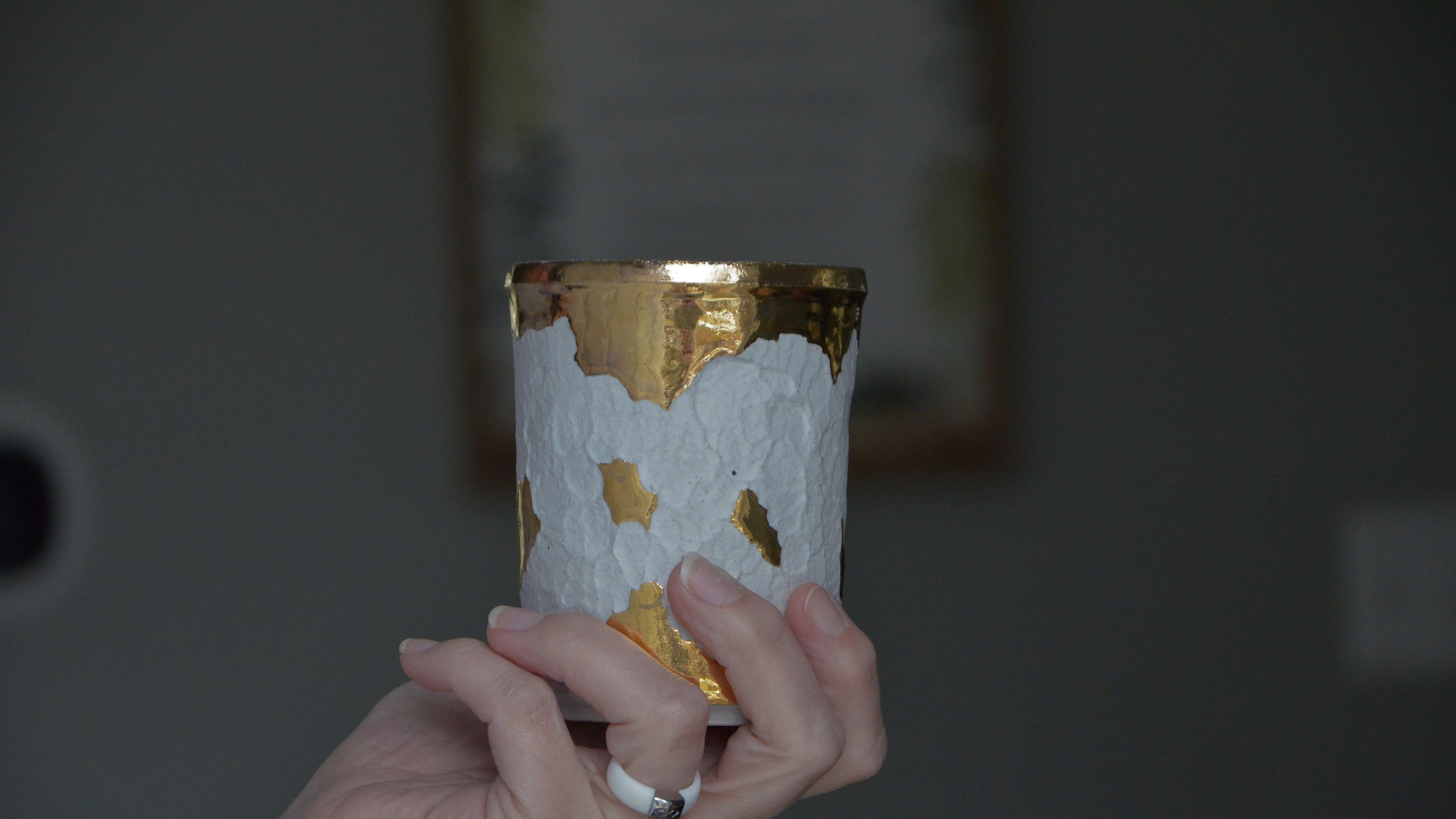 Hand holding a one of a kind white and gold ceramic cup inside 